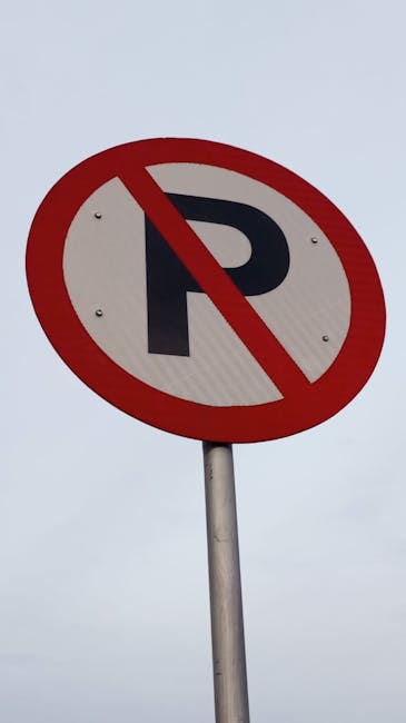 A round traffic sign mounted on a yellow wall, indicating no left or right turn with a red circle and diagonal line. The sign has a greyish-green background and features two protruding metal arrows pointing left and right, both of which are bent and attached to the sign. The sign appears weathered with some peeling paint around the edges. The setting suggests an exterior environment near a property or street, possibly adjacent to a loading area or pavement used for house removals. This type of signage is relevant in the context of logistics and moving operations, such as those provided by Man With a Van Primrose Hill, especially when adhering to local loading bay rules, as indicated by the page title.